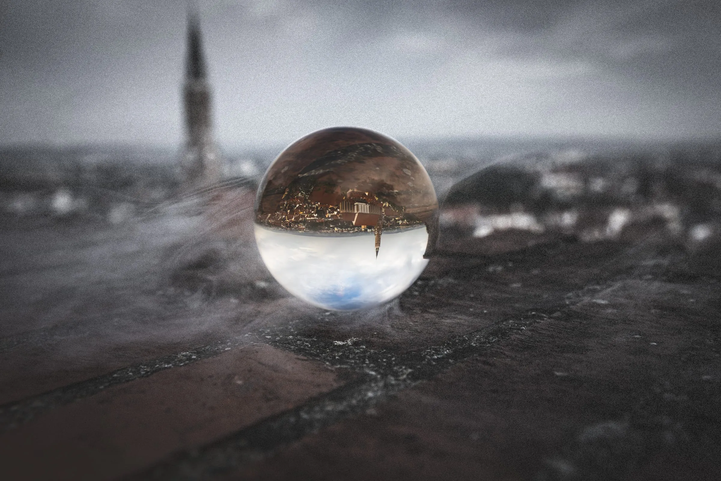 Glaskugel auf einer alten Ziegelmauer, in der die Altstadt mit dem Turm von St. Martin kopfüber erscheint; dahinter unscharf derselbe Turm unter grauem Himmel.